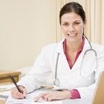 Doctor with laptop writing in doctor's office smiling